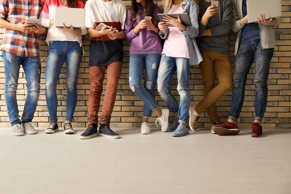 Group of cool teenagers with modern devices near brick wall — Stock Photo, Image