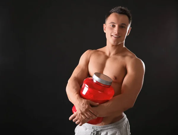 Jovem desportivo com frasco de proteína em pó sobre fundo preto — Fotografia de Stock