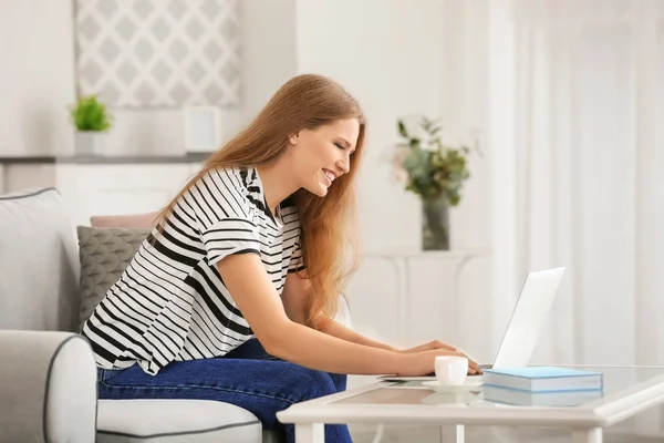 Belle femme utilisant un ordinateur portable tout en se reposant sur le canapé à la maison — Photo