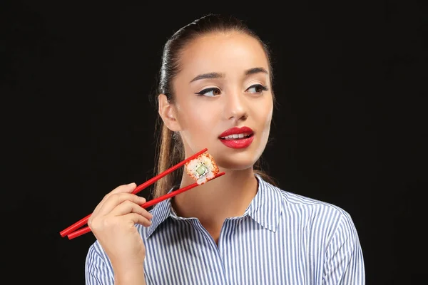 Mooie jonge vrouw met sushi roll op donkere achtergrond — Stockfoto