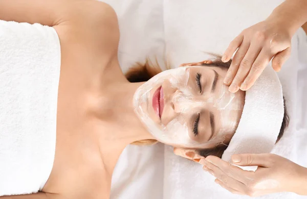 Beautician mengoleskan krim di wajah wanita muda di salon spa — Stok Foto
