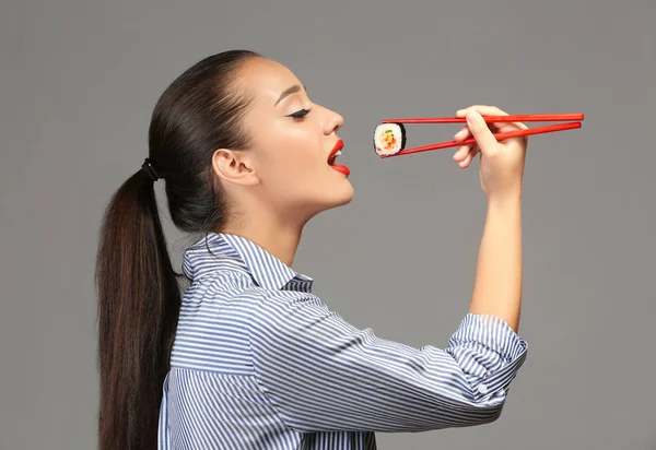 Beautiful young woman with sushi roll on grey background — Stock Photo, Image