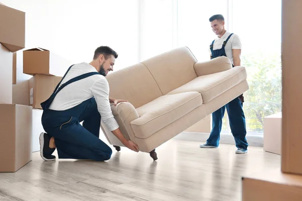 Entrega hombres moviendo sofá en la habitación en el nuevo hogar — Foto de Stock