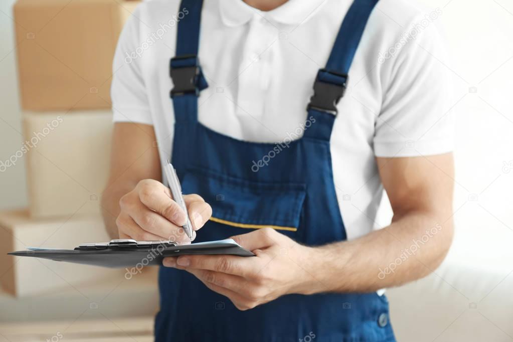 Delivery man checking list on clipboard indoors