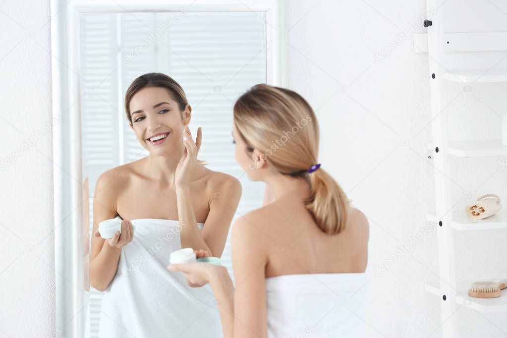 Young woman applying facial cream  