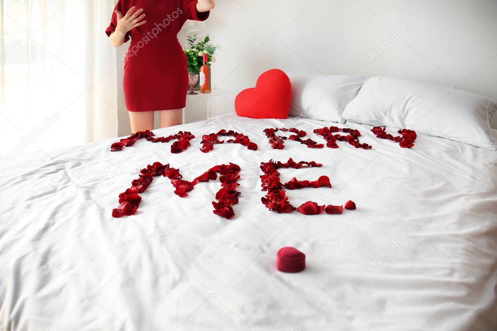 Idea for marriage proposal, message MARRY ME made of rose petals on bed and excited woman in room