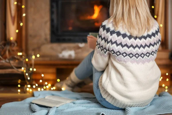 Mujer relajante cerca de la chimenea en la sala de estar decorada para vacaciones de invierno —  Fotos de Stock