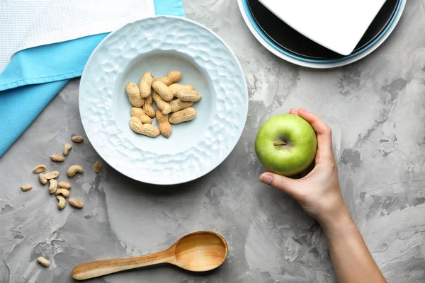 Жінка тримає яблуко і тарілку з арахісом на сірому фоні — стокове фото
