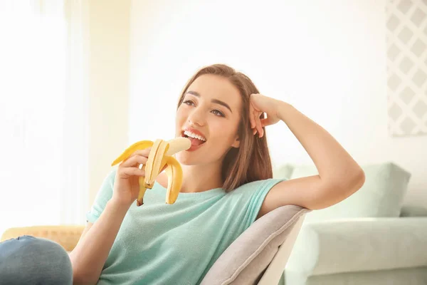 Attractive young woman eating banana indoors