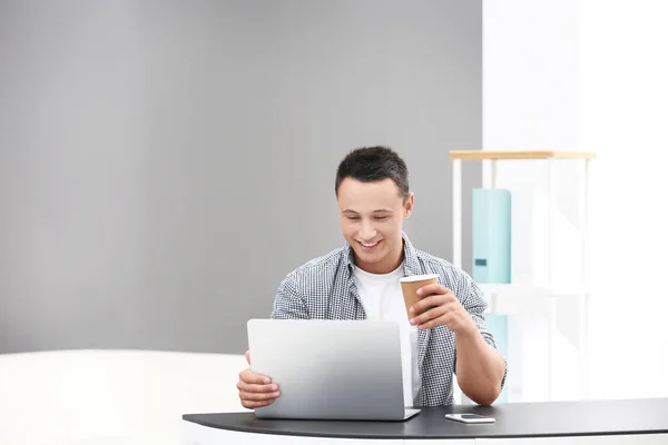 Jovem bebendo café e usando laptop no escritório — Fotografia de Stock