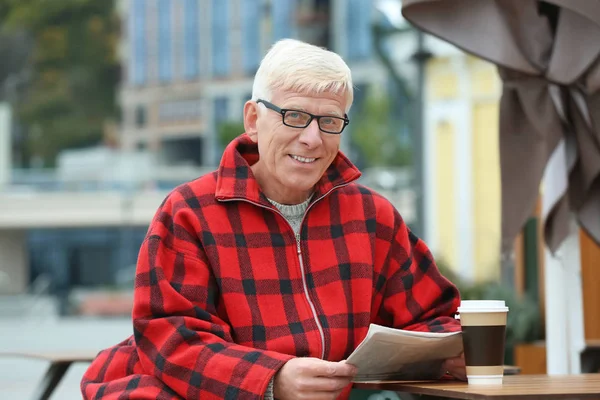 Knappe volwassen man met koffie en krant in café in openlucht — Stockfoto