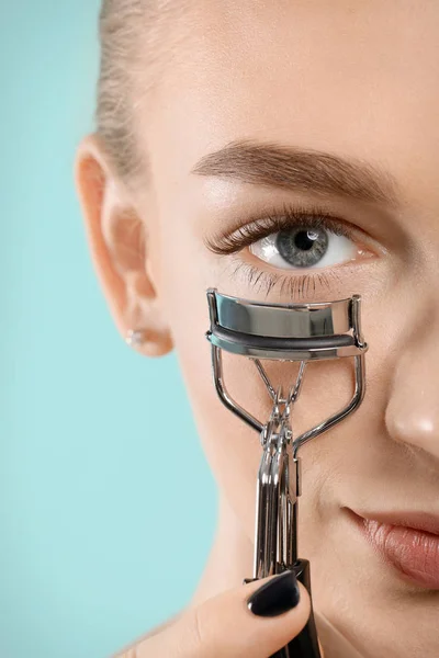 Beautiful young woman with eyelash curler on color background — Stock Photo, Image