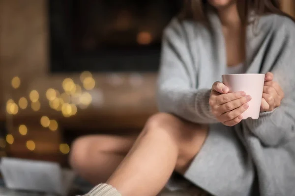 Mujer joven relajándose mientras bebe té en la sala de estar decorada para las vacaciones de invierno — Foto de Stock