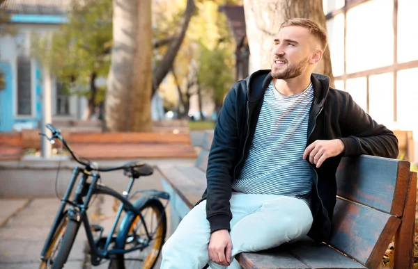 Knappe jonge hipster man met fiets zitten op bankje buiten — Stockfoto
