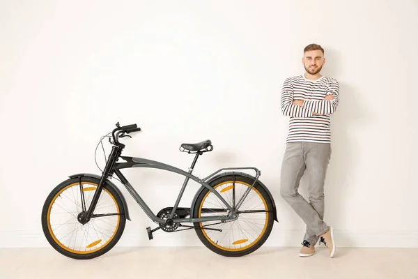 Guapo joven hipster hombre con bicicleta cerca de la pared de luz —  Fotos de Stock