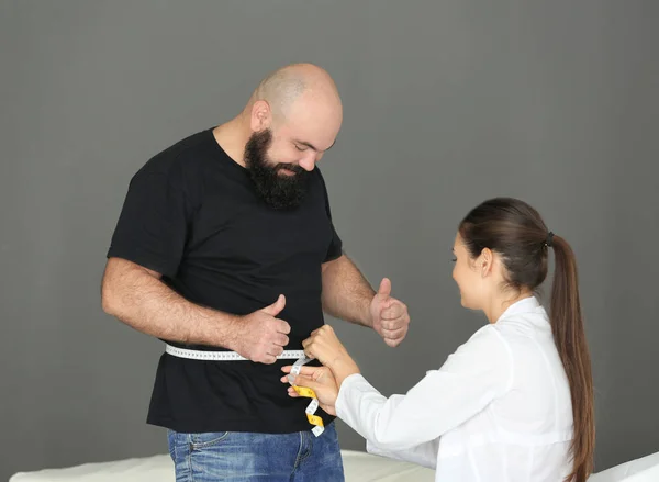 Mujer joven médico que mide la cintura del hombre con sobrepeso con centímetro en la clínica — Foto de Stock