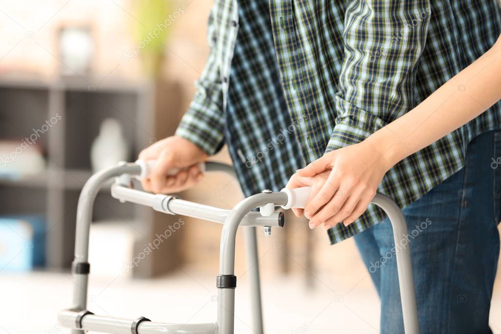 Senior man with walking frame and young caregiver, indoors