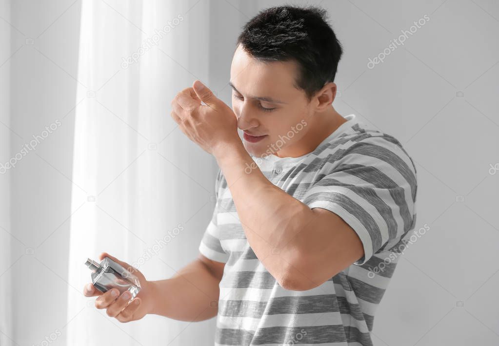 Handsome young man using perfume at home