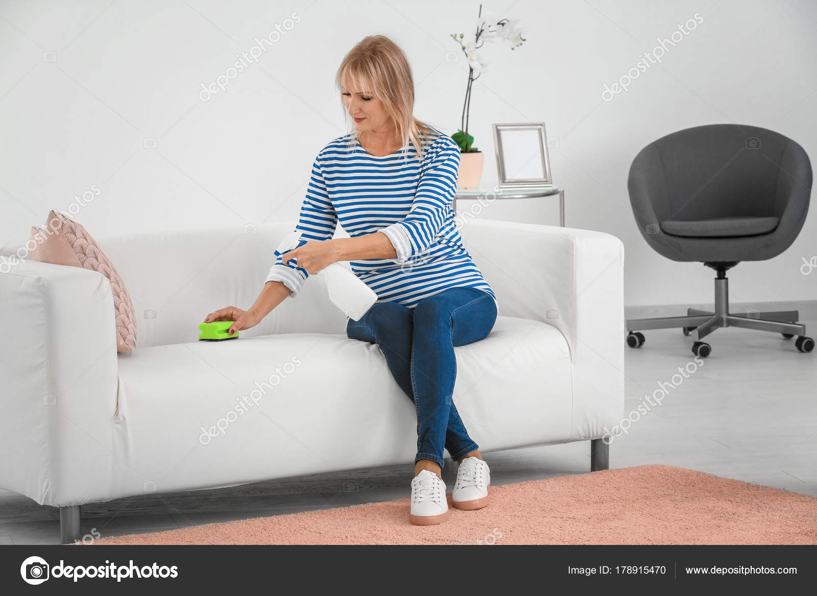 Mature woman cleaning sofa at home Stock Photo by ©belchonock