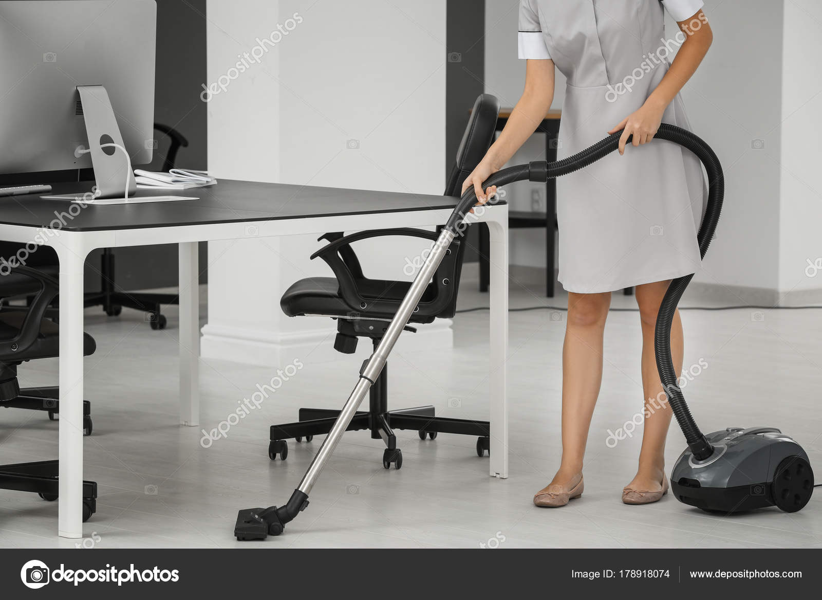 Young Woman Hoovering Floor In Office Using Vacuum Cleaner Stock