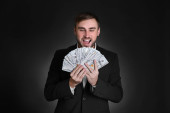Šťastný muž v formálním obleku s penězi na černém pozadí. Burze makléř