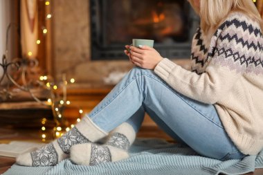 Genç kadın oturma odasında çay yudumlarken rahatlatıcı kış tatilleri için dekore edilmiştir.