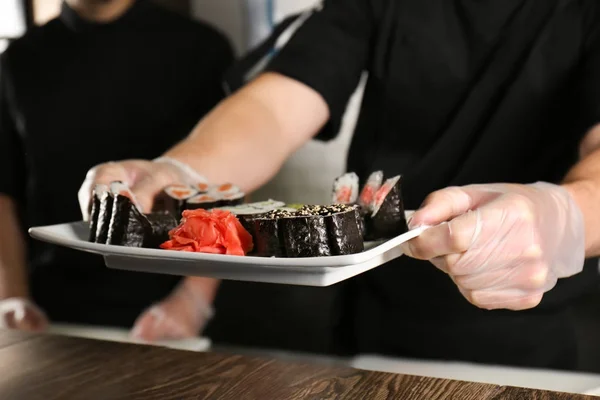 Chef con plato de deliciosos rollos maki en restaurante — Foto de Stock