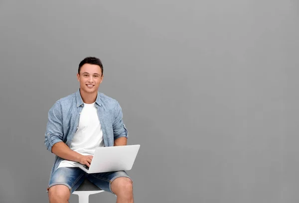 Młody człowiek z laptopa siedząc na krześle koło szare ściany — Zdjęcie stockowe