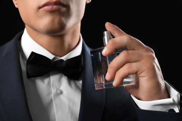 Knappe jonge man in pak met behulp van parfum op zwarte achtergrond — Stockfoto