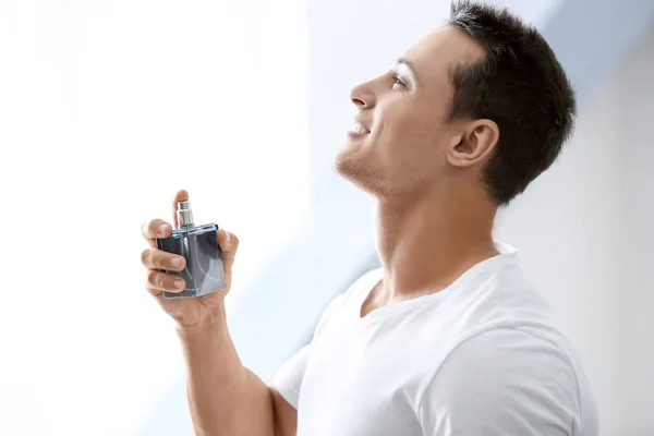 Bonito homem com garrafa de perfume no fundo claro — Fotografia de Stock