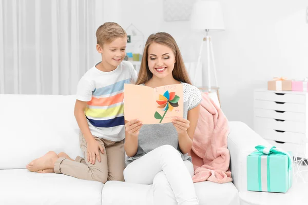 Mujer joven con su hijo pequeño y tarjeta de felicitación para el Día de la Madre en casa — Foto de Stock