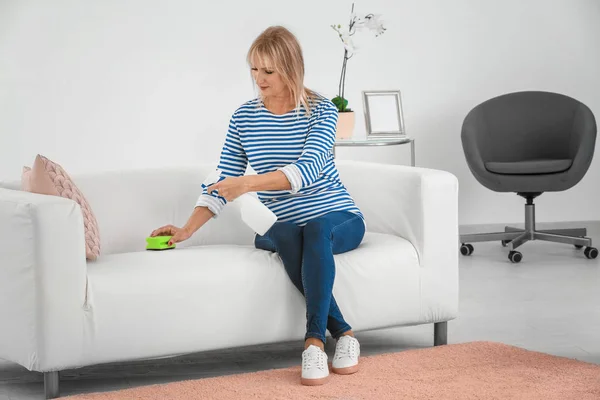 Mature woman cleaning sofa at home