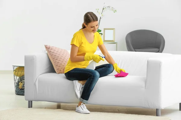 Молодая женщина убирает диван дома — стоковое фото