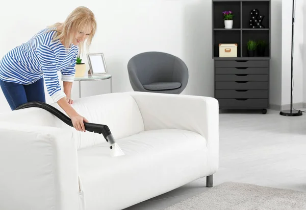 Mulher madura removendo sujeira do sofá usando aspirador de pó — Fotografia de Stock