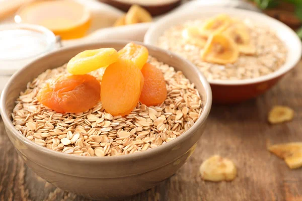 Bowl with oatmeal flakes and dried apricots on wooden background — Stock Photo, Image