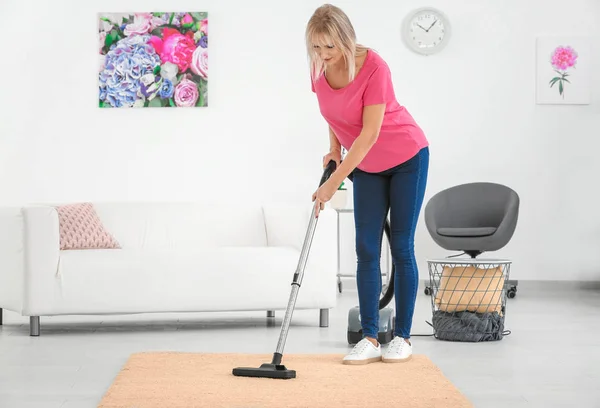 Alfombra de hoovering mujer madura con aspiradora en casa — Foto de Stock