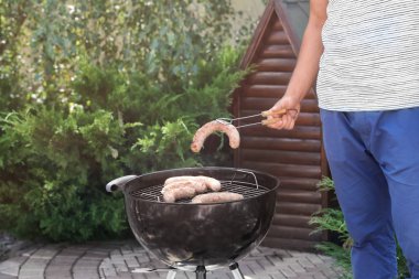 Adam açık havada mangal üzerinde lezzetli sosis hazırlanıyor