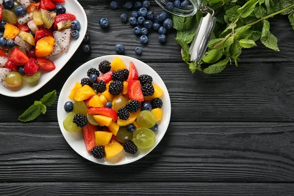 Pratos com deliciosa salada de frutas na mesa de madeira — Fotografia de Stock