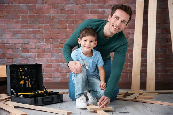 Father teaching his little son to drive nail in workshop