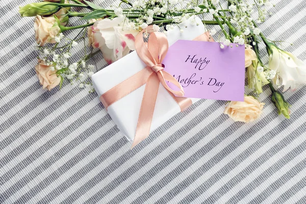 Cartão com palavras "Feliz Dia das Mães", caixa de presente e flores em pano listrado, vista superior — Fotografia de Stock