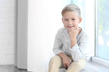 Pencere kenarında oturan sevimli moda çocuk