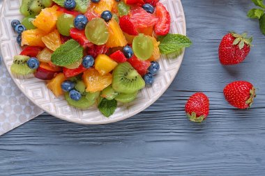 Ahşap masa üzerinde lezzetli meyve salatası ile plaka