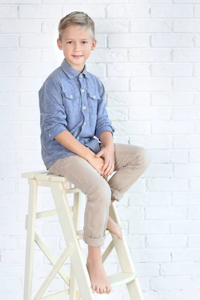 Bonito menino da moda sentado na escada perto da parede de tijolo branco — Fotografia de Stock