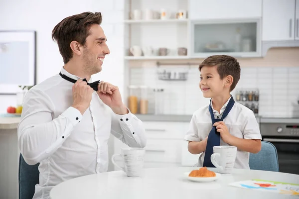 Padre con hijo poniéndose corbata y corbata mientras desayunaba en la cocina — Foto de Stock