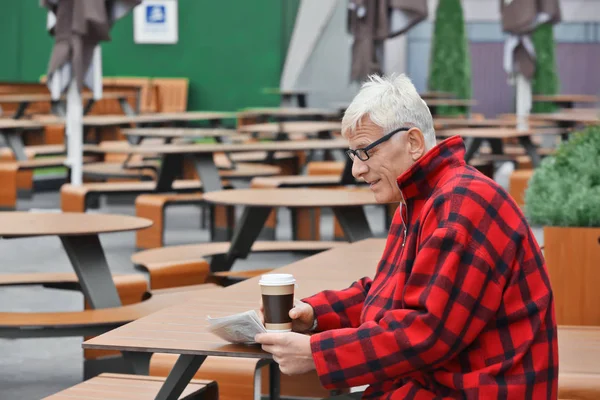 Krásný zralý muž s kávou a noviny v café venku — Stock fotografie