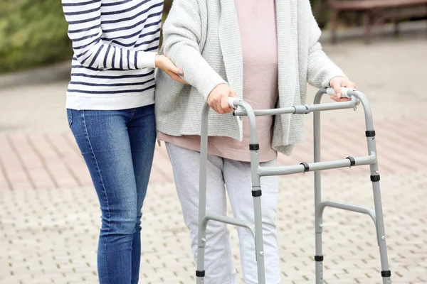 Jonge vrouw en haar bejaarde oma met frame buiten wandelen — Stockfoto