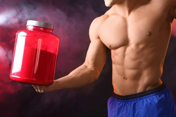 Sportlicher junger Mann mit einem Glas Proteinpuder auf dunklem Hintergrund — Stockfoto