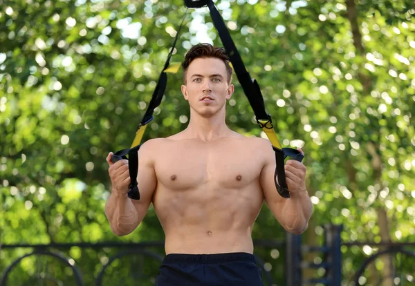 Bonito jovem musculoso exercitando com tiras TRX ao ar livre — Fotografia de Stock