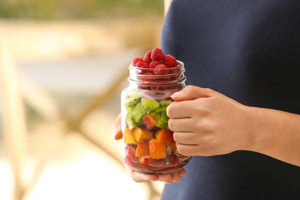 Woman holding mason jar with fruits and berries on blurred background — Stock Photo, Image