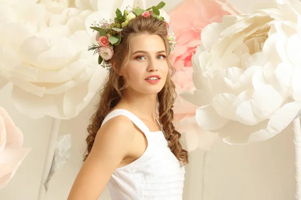 Hermosa mujer joven cerca de flores artificiales decorativas sobre fondo claro —  Fotos de Stock